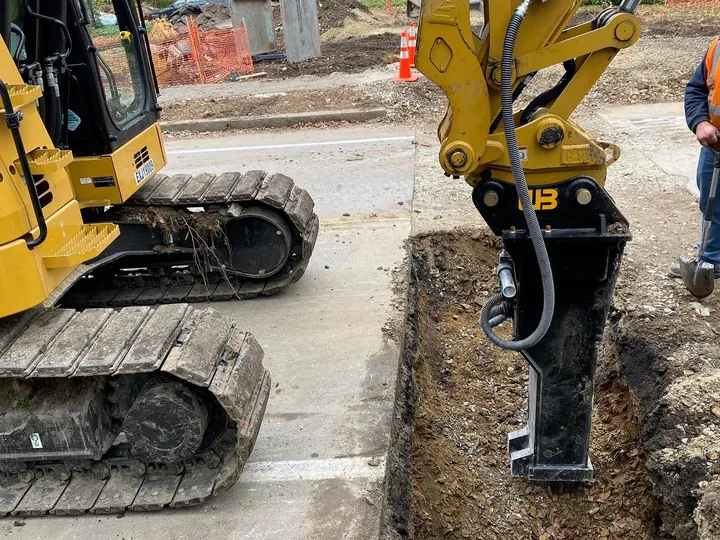 Excavator breaker cutting in next to a curb and sidewalk
