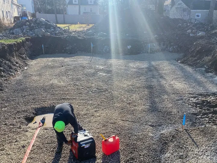 Crew member compacting a gravel base inside an excavated site