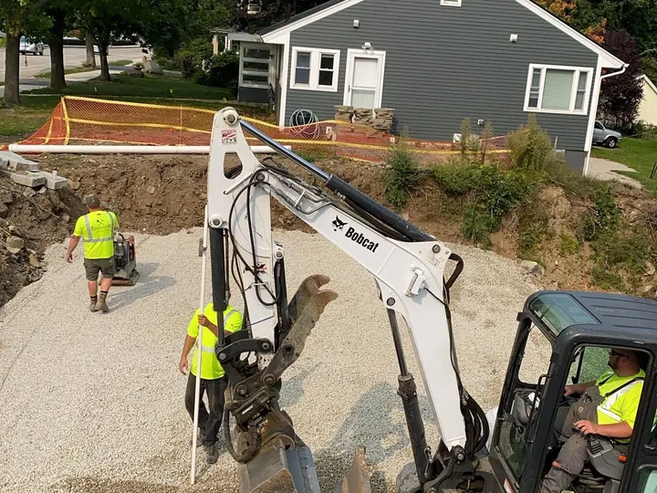 Gravel being spread beside a house with a mini excavator