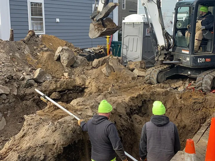 Crew in a trench along the side of a gray house