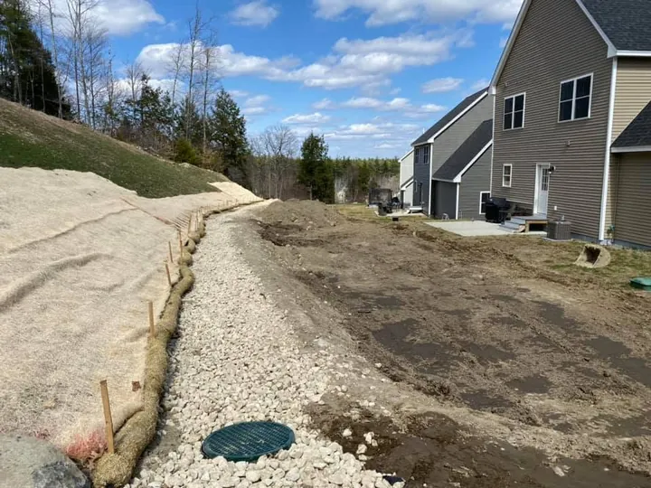 Stone lined drainage swale with a green catch basin below a slope
