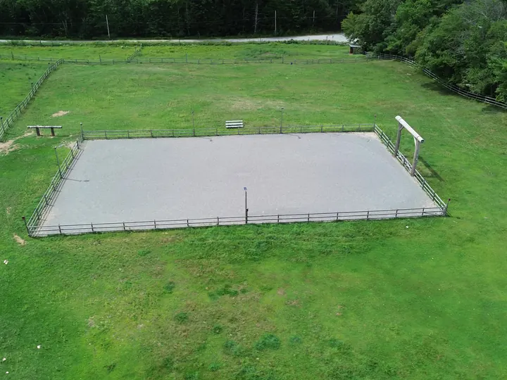 Aerial view of a finished gravel riding arena pad with fencing in an open field