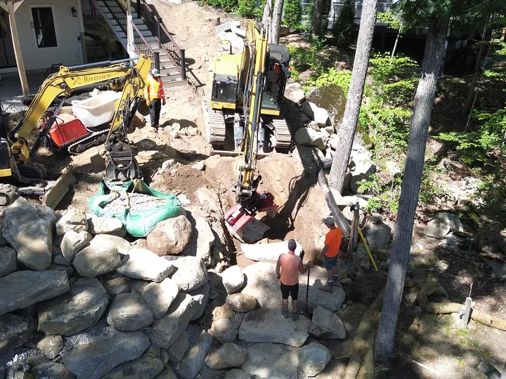Drone view of crew and machines working among large boulders beside a house