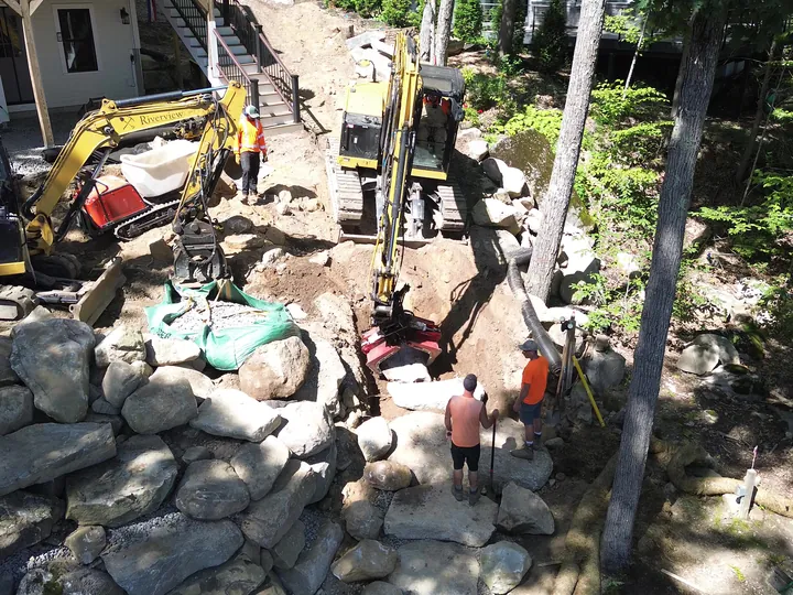 Drone view of crew and a machine working between large boulders