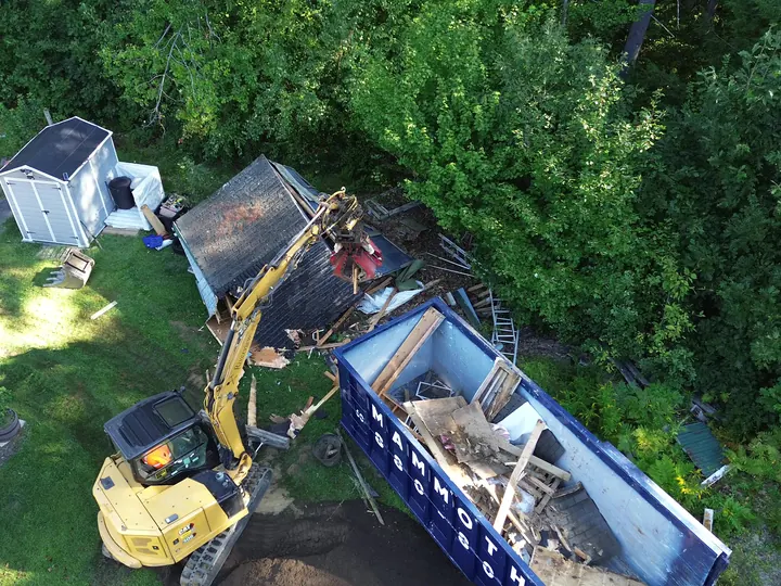 Aerial view of an excavator loading shed debris into a dumpster