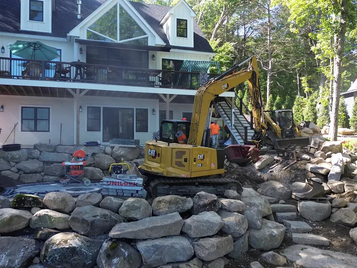 Drone view of an excavator on a boulder slope below a house
