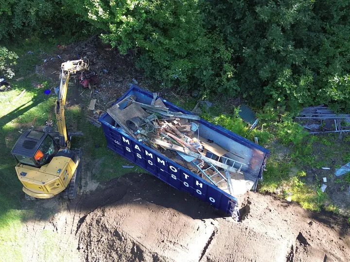 Drone view of an excavator between a pile of soil and a dumpster in a yard