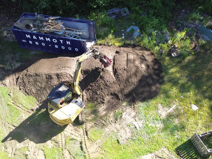 Drone view of an excavator beside a large pile of dug soil in a backyard