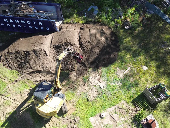Drone view of an excavator beside a tall pile of dirt in a yard