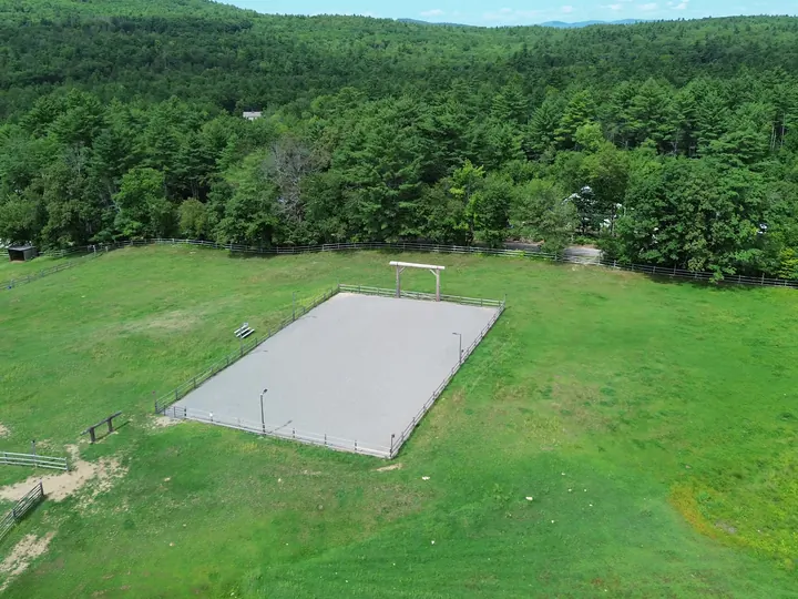 Aerial view of a graded gravel pad in a grassy field with woods behind it