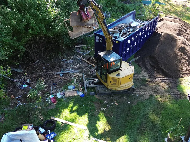Aerial view of an excavator grapple picking up debris beside a dumpster