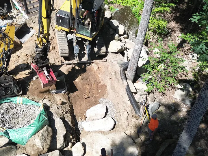 Top down drone view of a grapple placing stone as the crew stands by