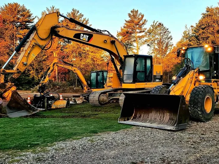 Full size excavator and wheel loader parked on a lawn under fall foliage