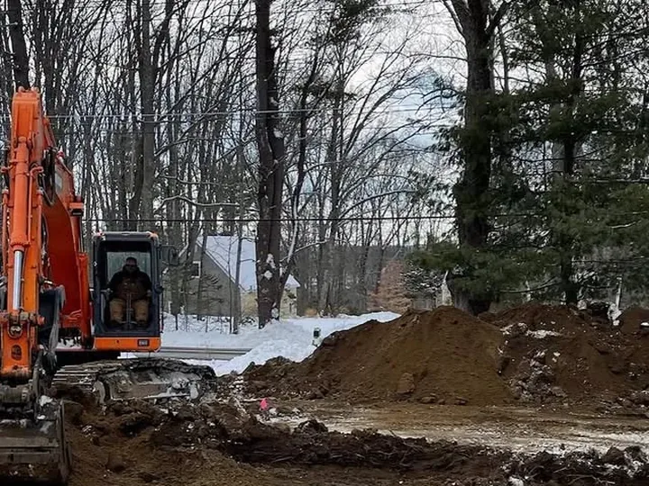 Orange excavator on a cleared winter lot during a leach field replacement