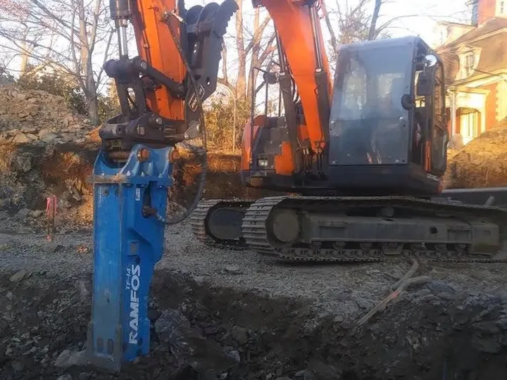 Excavator running a blue hydraulic hammer down in a trench