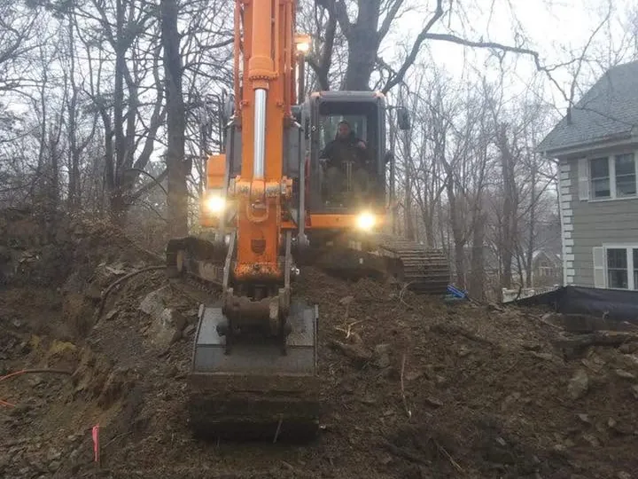 Orange excavator with its lights on working a dig in the evening