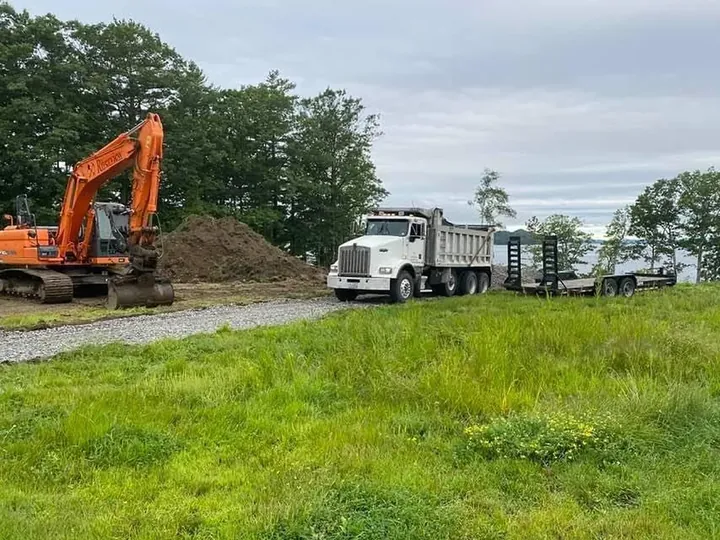 Orange excavator and a dump truck parked by a dirt pile on a grassy lot