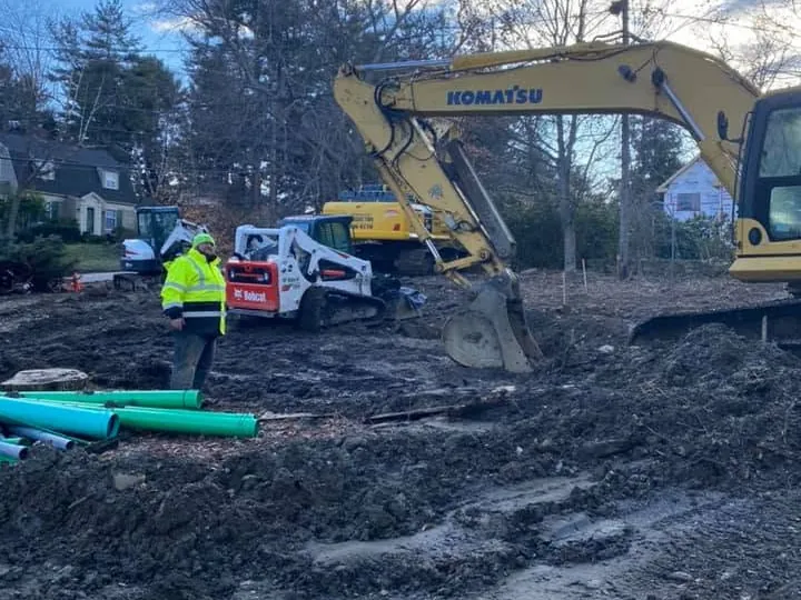 Wet dirt lot with an excavator and a stack of green pipe