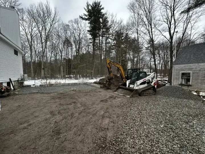 Graded gravel pad beside a house with a track loader on site