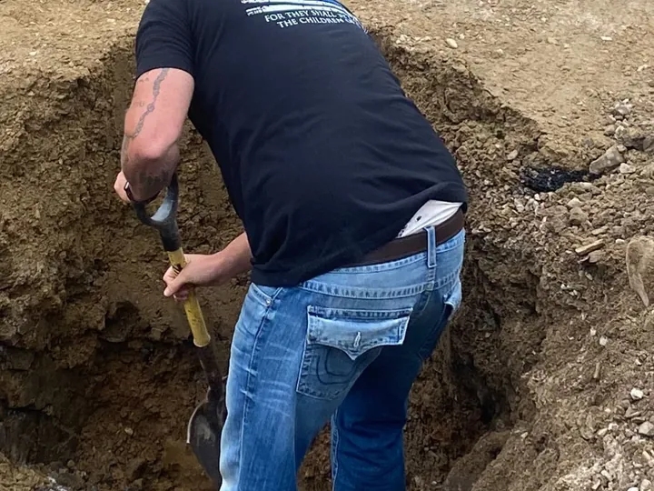 Crew member digging by hand inside a deep hole