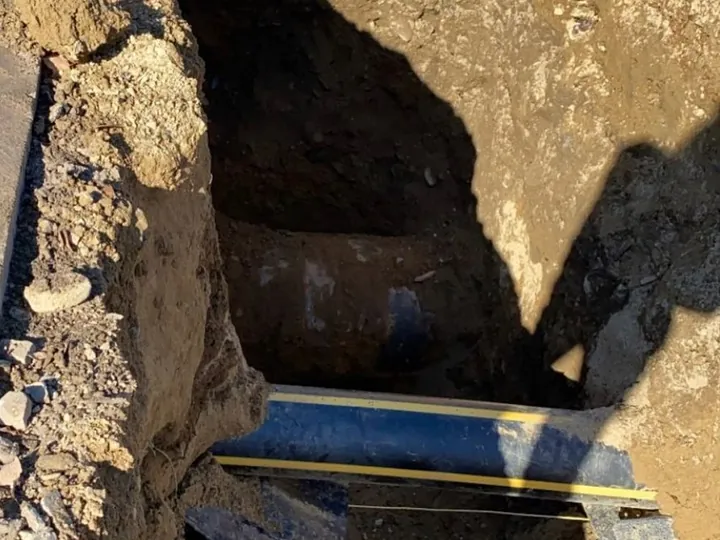 Large existing pipe exposed in a trench with a striped line running beneath it