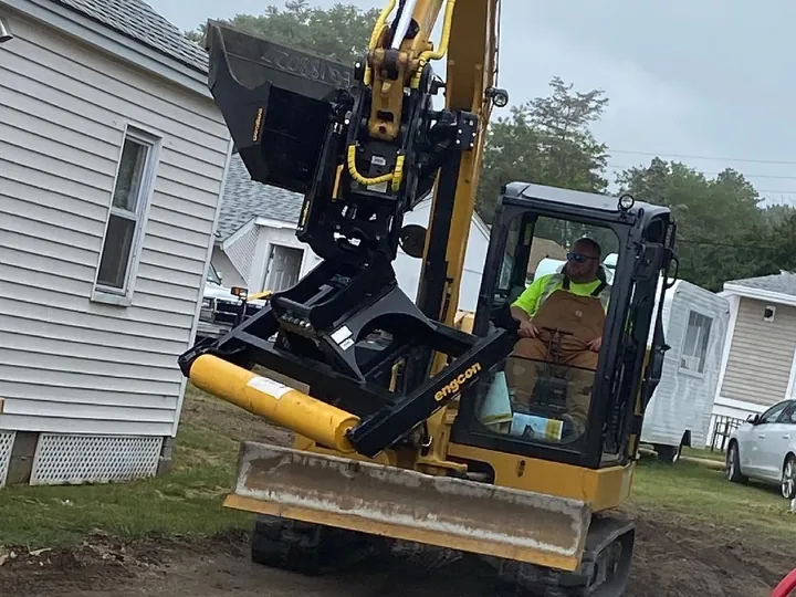 Compact excavator with a tilting bucket working tight to a house