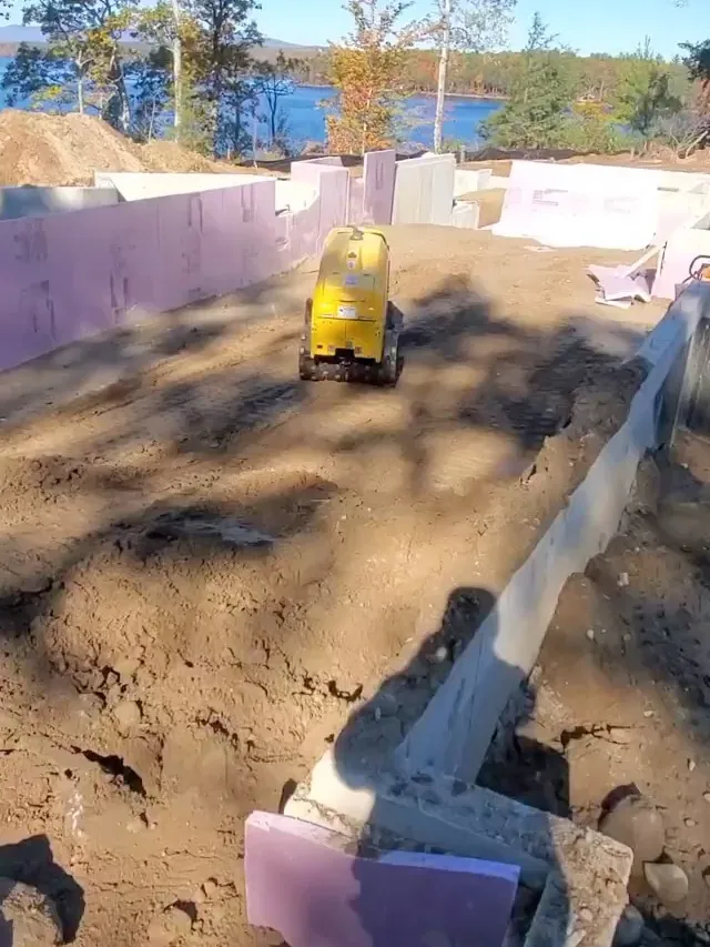 Plate compactor backfilling inside new foundation walls with the lake behind