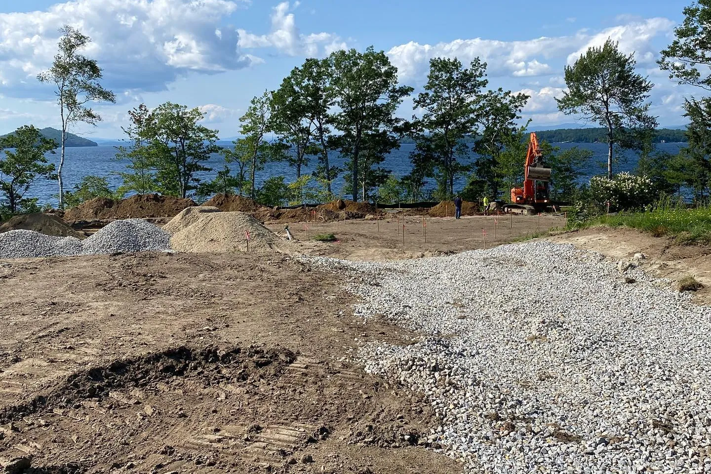 Staked out home site with a new gravel drive and an excavator working at the edge of the lake in Alton Bay