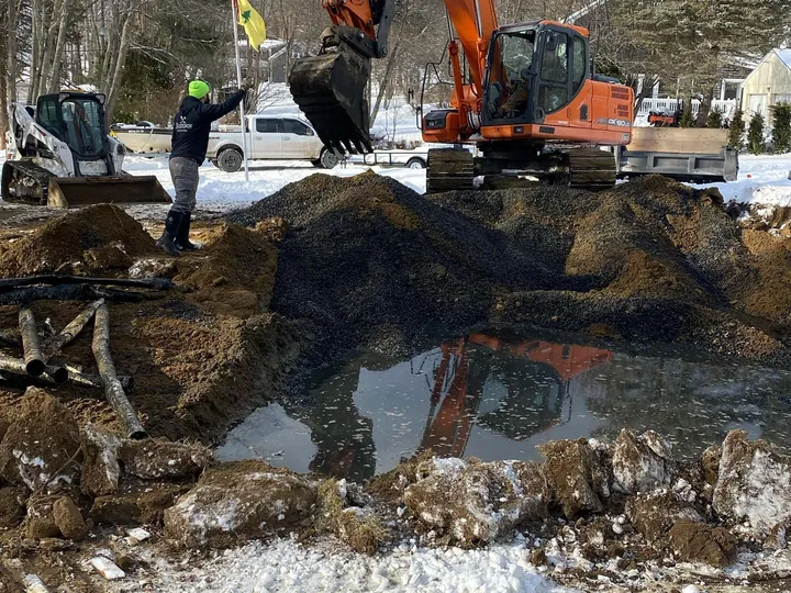 Excavator digging beside standing water at a septic repair