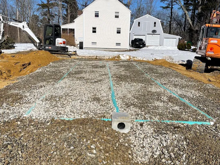 Finished septic field of crushed stone and pipe runs in front of a house