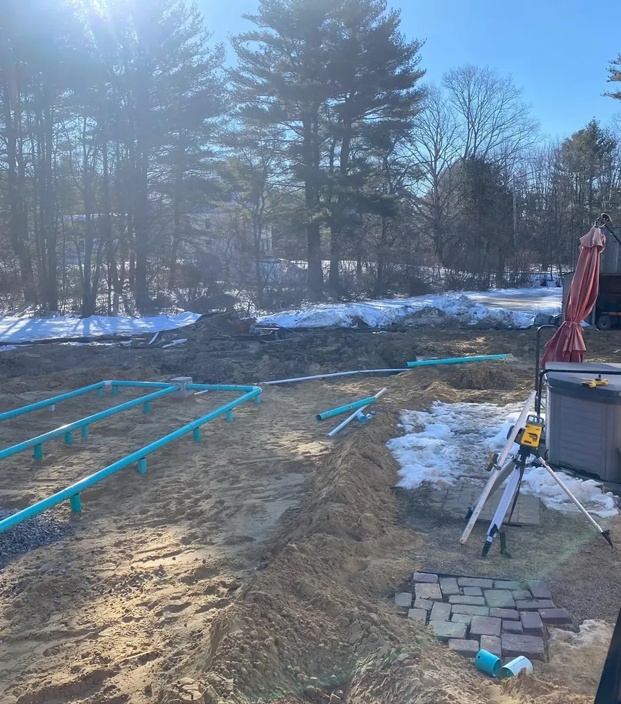 Pipe runs laid out in an open trench bed, with a laser level set up beside them