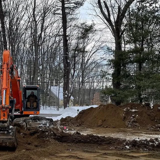 Orange excavator beside a snowbank on a winter leach field job