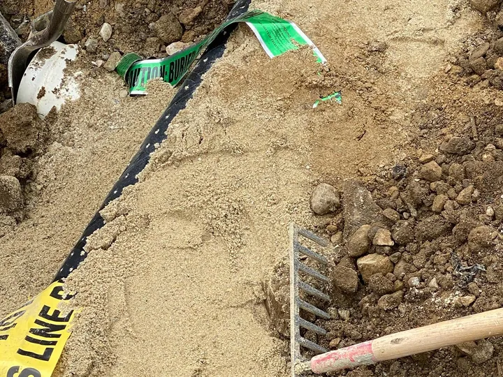 New sewer pipe in a trench beside a gas line marked with yellow tape