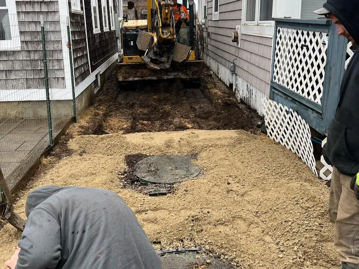 Crew member kneeling in a tight dig beside a house