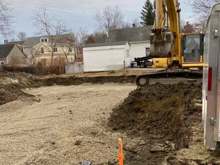 Excavator cutting a trench beside a gravel pad between houses