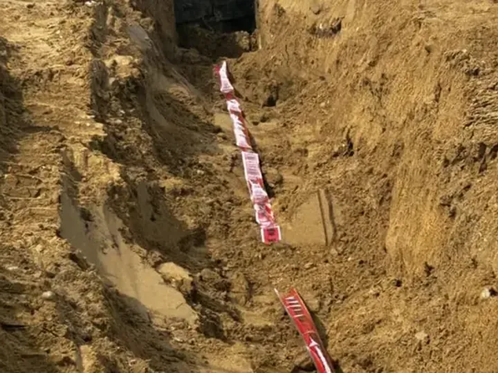 Deep utility trench with red warning tape running along the pipe